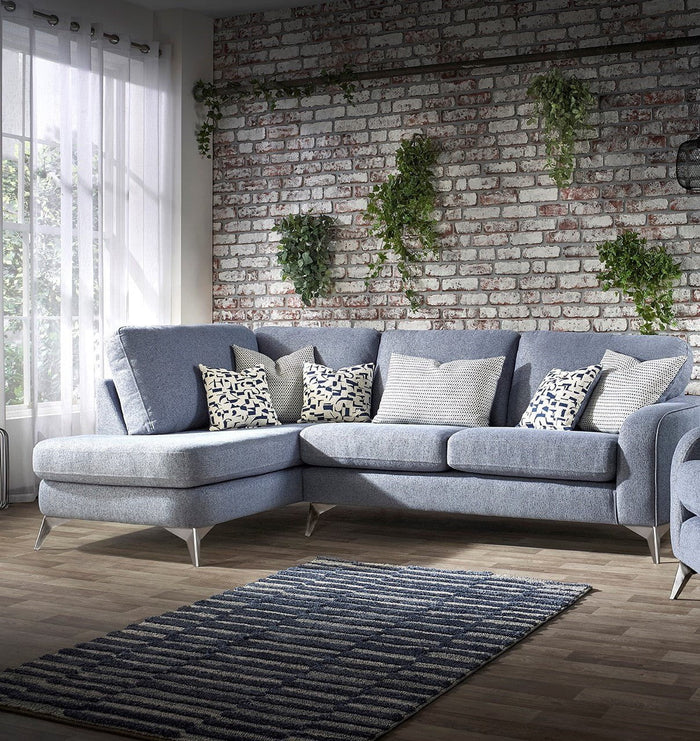 Gray sectional sofa with patterned cushions in a room with a brick wall and plants.
